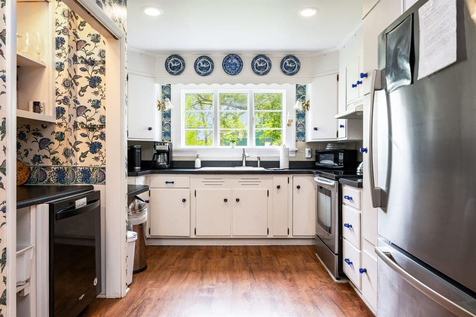 Charming vintage kitchen with modern stainless steel appliances, classic blue accents, and a scenic view above the sink 🌿🍽️💙