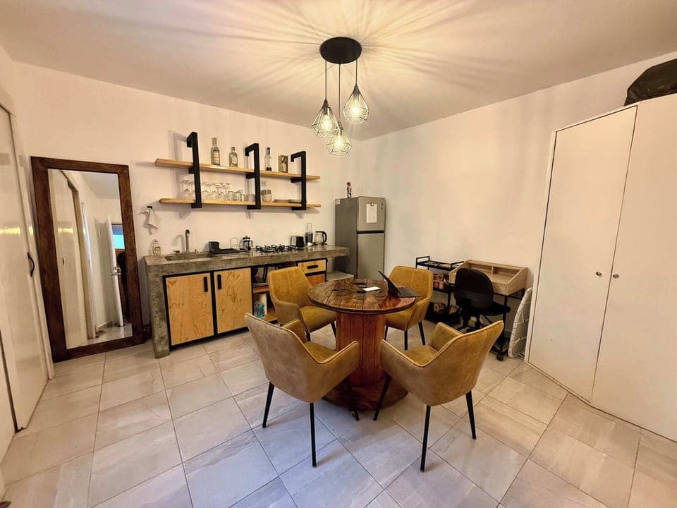 Sala (mesa con 4 sillas, escritorio individual con silla, lámpara de lectura, cocina integrada, espejo alto, clóset, barra con estufa integrada, tarja, repisas con tazas, copas y licores, refrigerador, stand con snacks, minibar)
