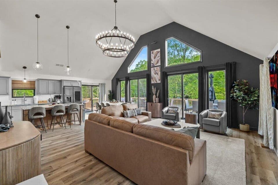 Sunlight pours through floor-to-ceiling windows into the vaulted living room with views of the deck.