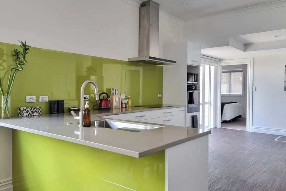 The large modern kitchen has a lime green splashback, an island bench with twin sinks, a built-in oven, and a microwave.