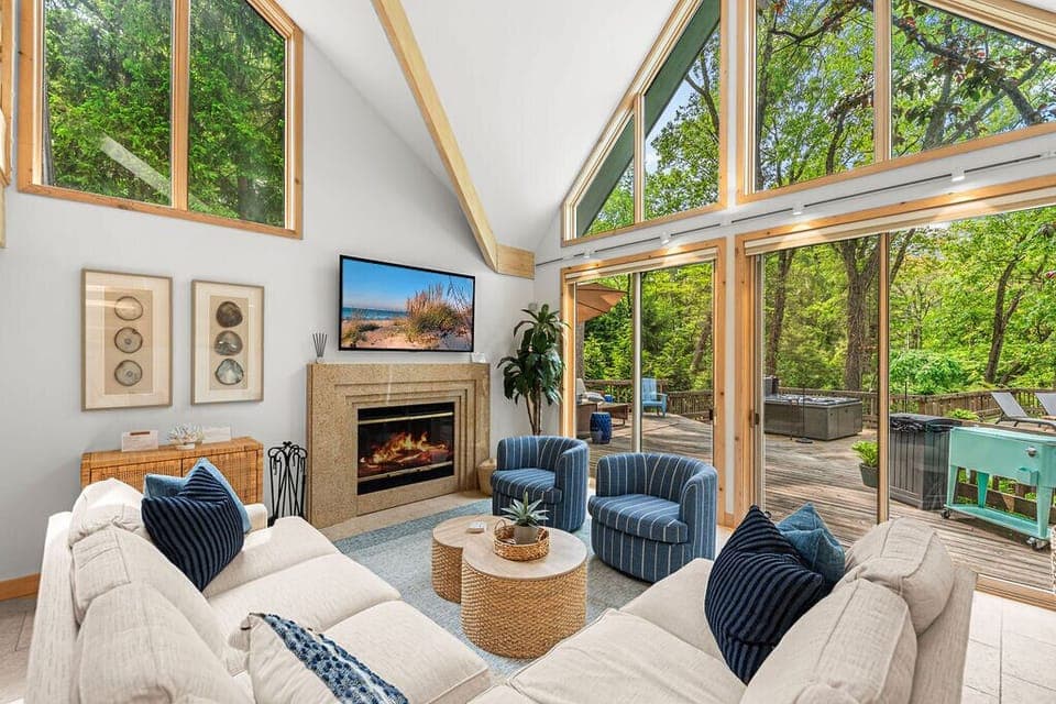 Wall of windows, fireplace glow, and forest all around.