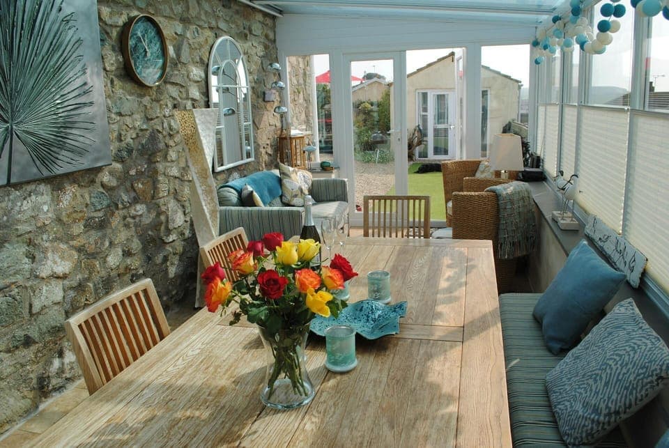 dining table with vase of flowers, sofa and chairs in the conservatory