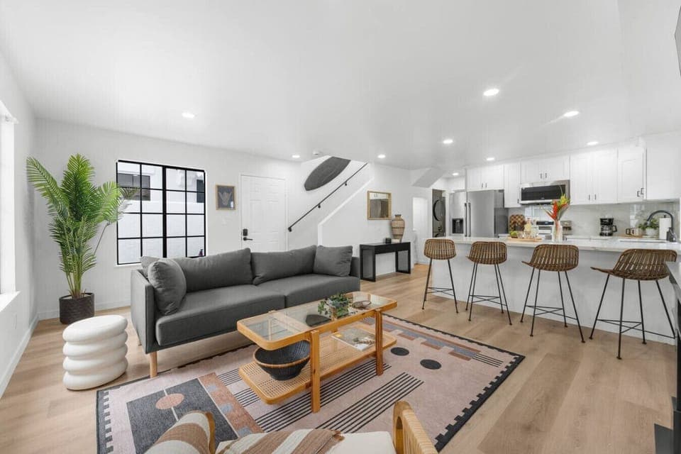 A modern coastal retreat in Crown Point, this open living area features a plush sectional, surf-inspired decor, and a breakfast bar—perfect for morning coffee before a short walk to the bay or a relaxing San Diego vacation evening in.