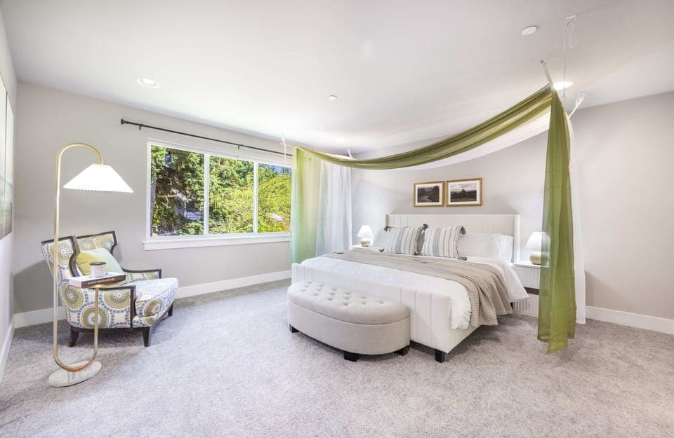 The green canopy drapes elegantly over the bed, while a geometric-patterned armchair and gold floor lamp create a cozy reading nook by the plant-filled window.