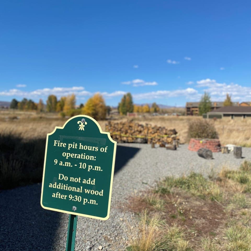 Fire pit area with posted hours and autumn landscape nearby.