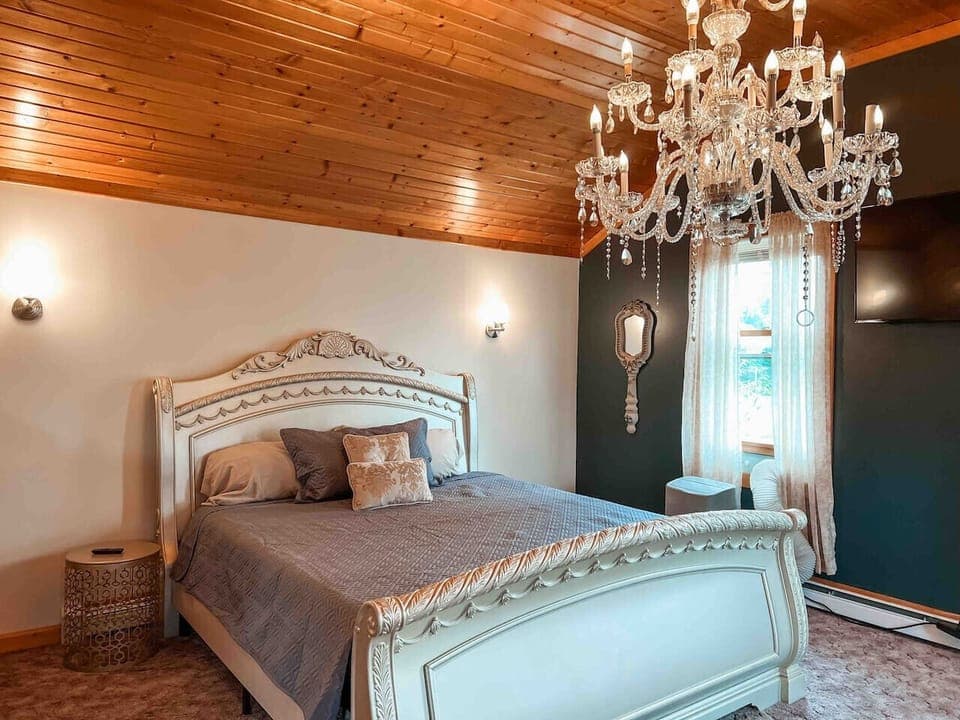 Sleep beneath a sparking chandelier in this elegant king bed, where warm wood ceilings meet luxurious finishes for a truly timeless retreat.