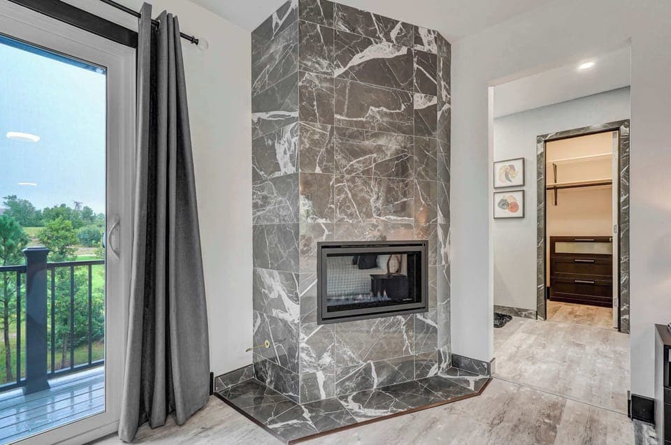 Elegant double-sided fireplace in the primary suite with access to the balcony and walk-in closet beyond.
