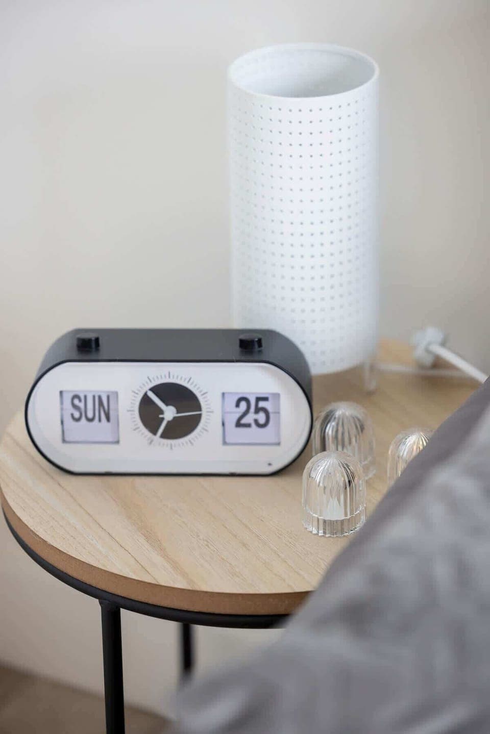 A small round bedside table holding a digital clock.