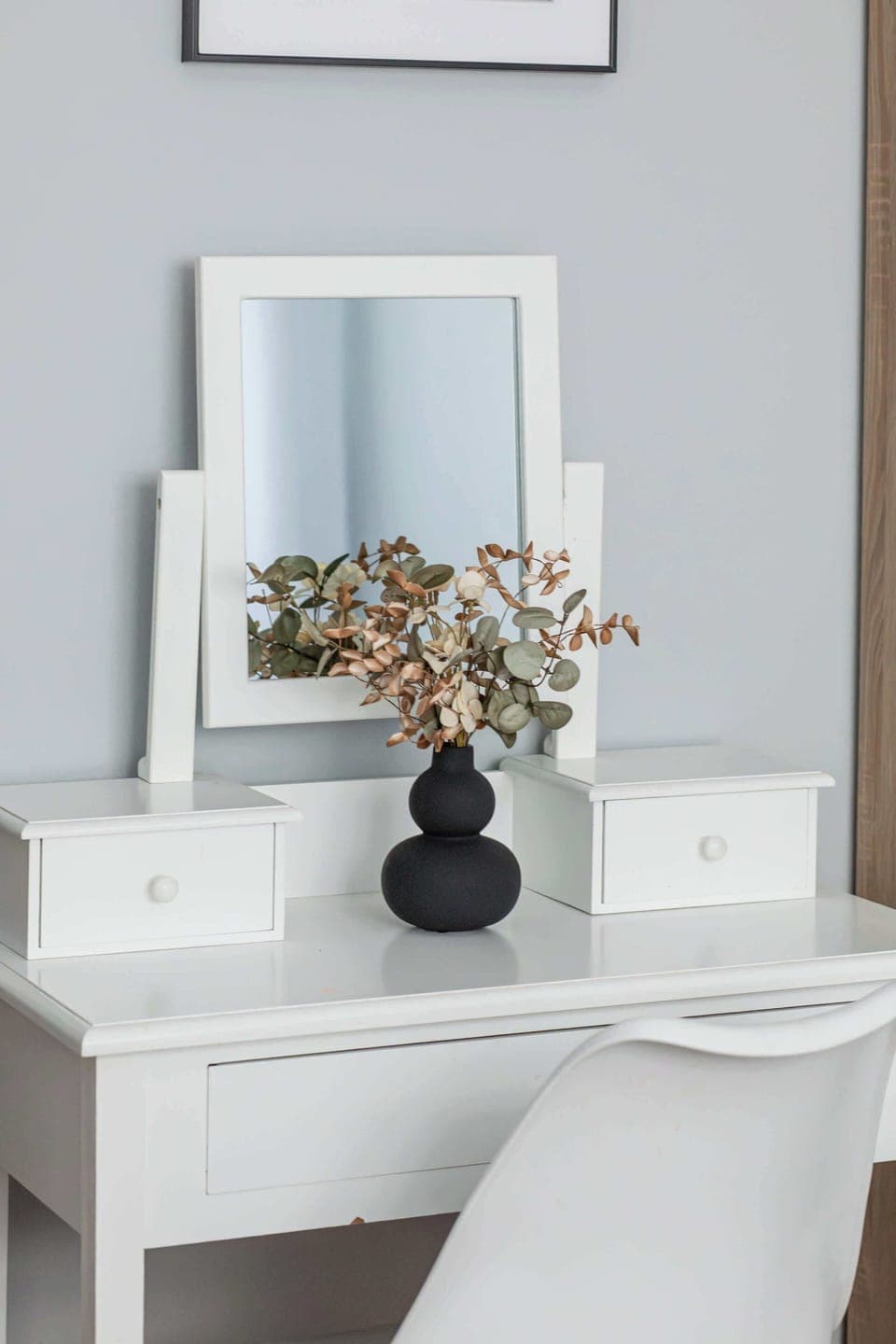 A white dressing table with a mirror and a decorative flower arrangement. Adds a touch of elegance and functionality to the space.