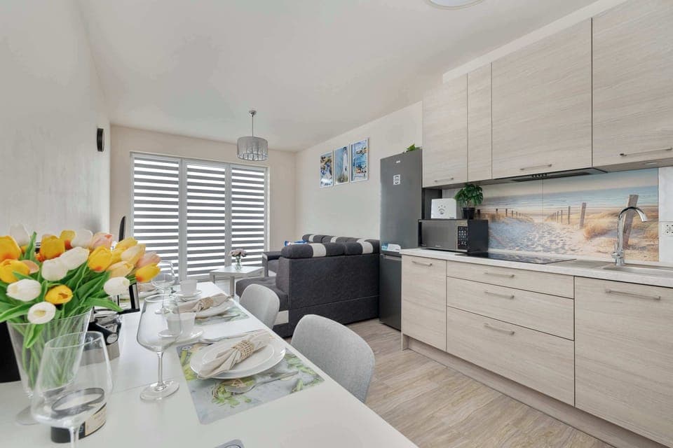A kitchen and dining area with light wood cabinets, tulips in a vase, and a neatly set table for four people.
