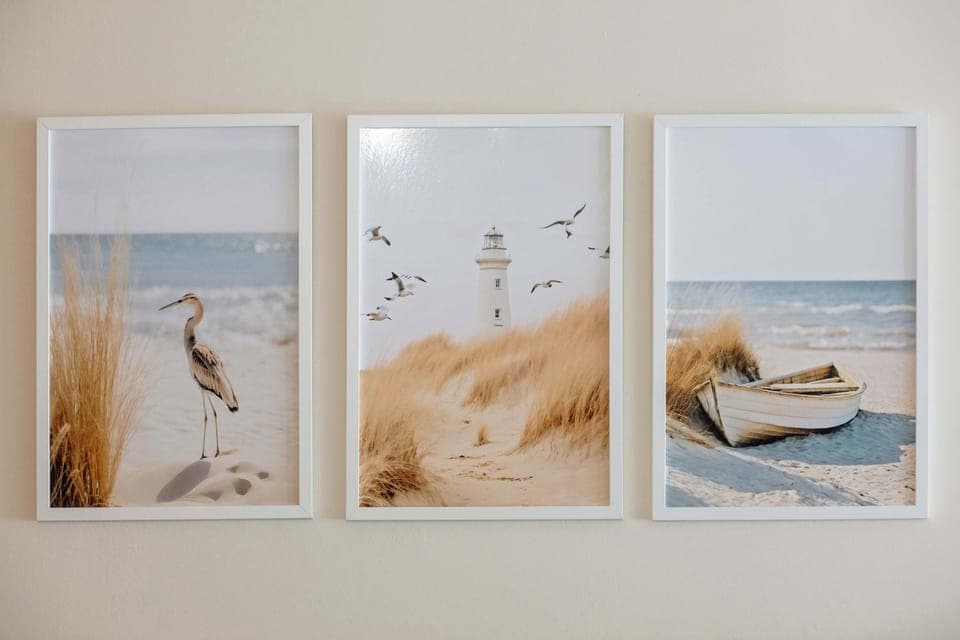 A minimalist wall art arrangement featuring three canvas prints of beach and seagull scenes.