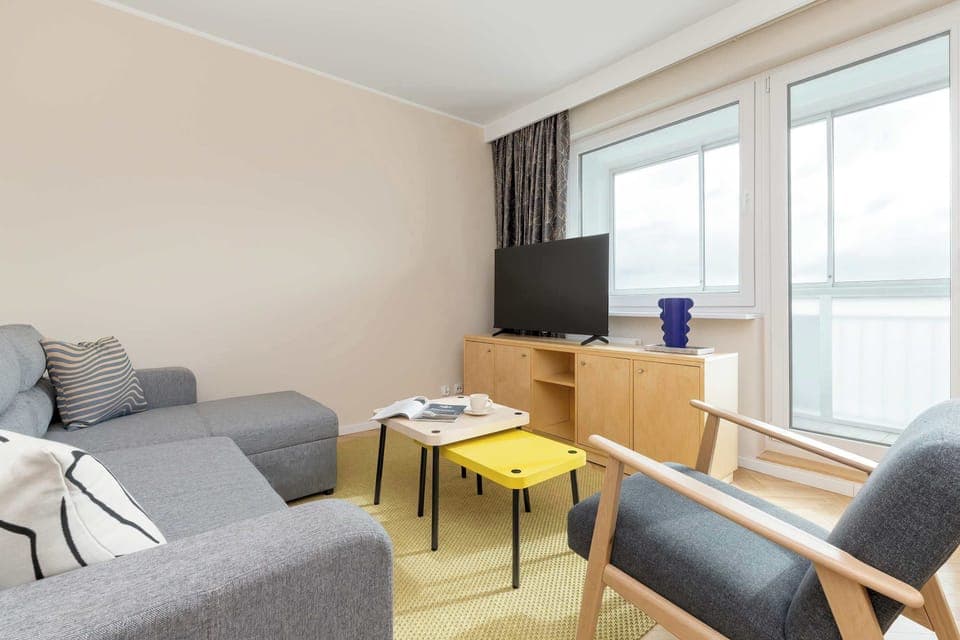 A bright living space with a sofa bed, armchair, and coffee table, decorated in modern neutral tones.