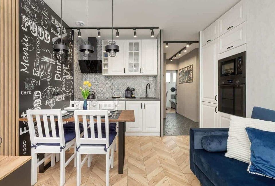 A contemporary kitchen with white cabinetry, patterned backsplash, and stainless steel appliances. The open layout connects seamlessly to the living room.