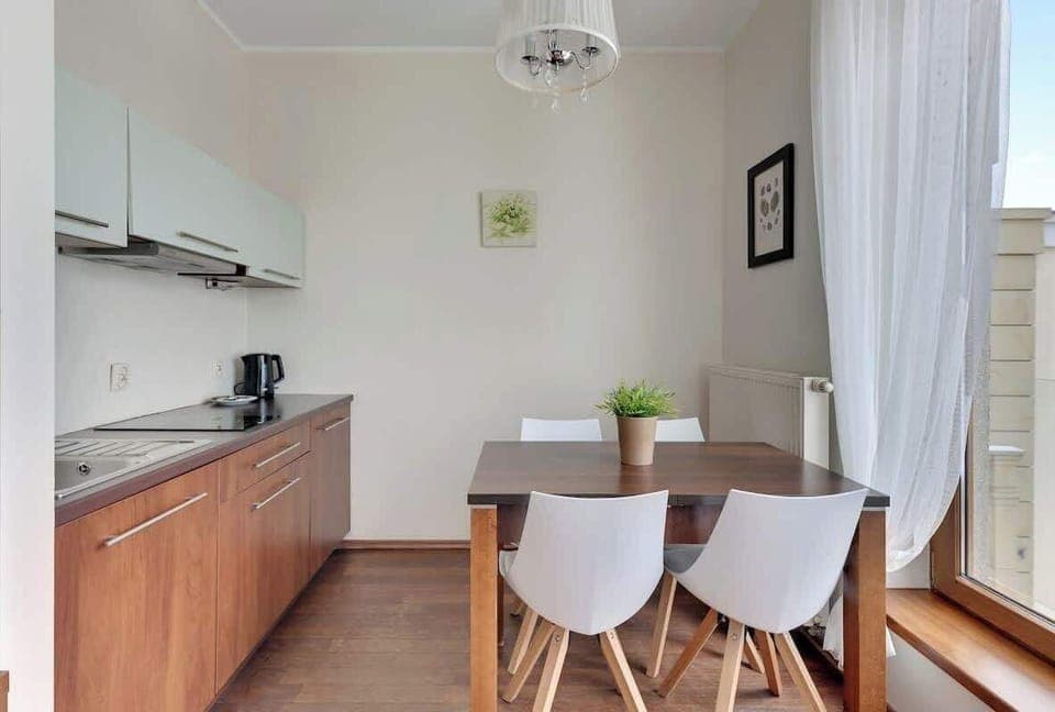 A sleek kitchen with a wooden dining table, contemporary chairs, and a well-organized layout, offering a warm and inviting cooking space with natural light coming in from the windows.