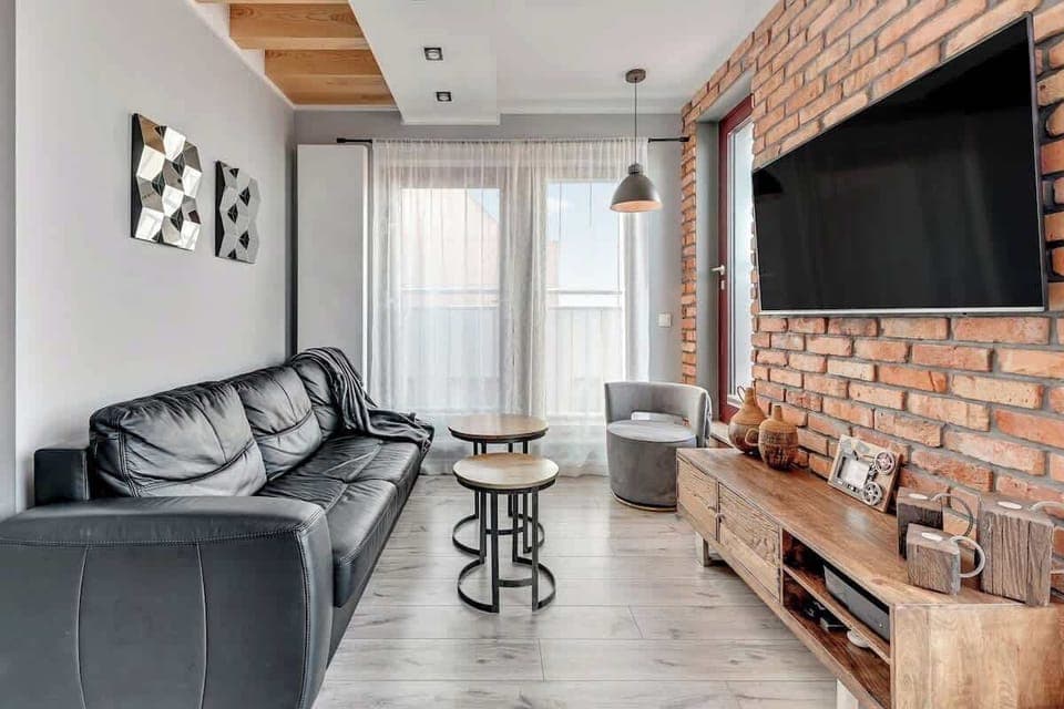 A cozy living area with modern black leather furniture, exposed brick walls, and a flat-screen TV, creating a trendy industrial vibe.