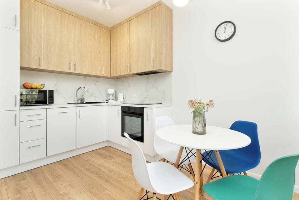Well-equipped kitchen with wooden upper cabinets, black appliances, and a light dining space. The combination of textures creates a warm and practical cooking environment.