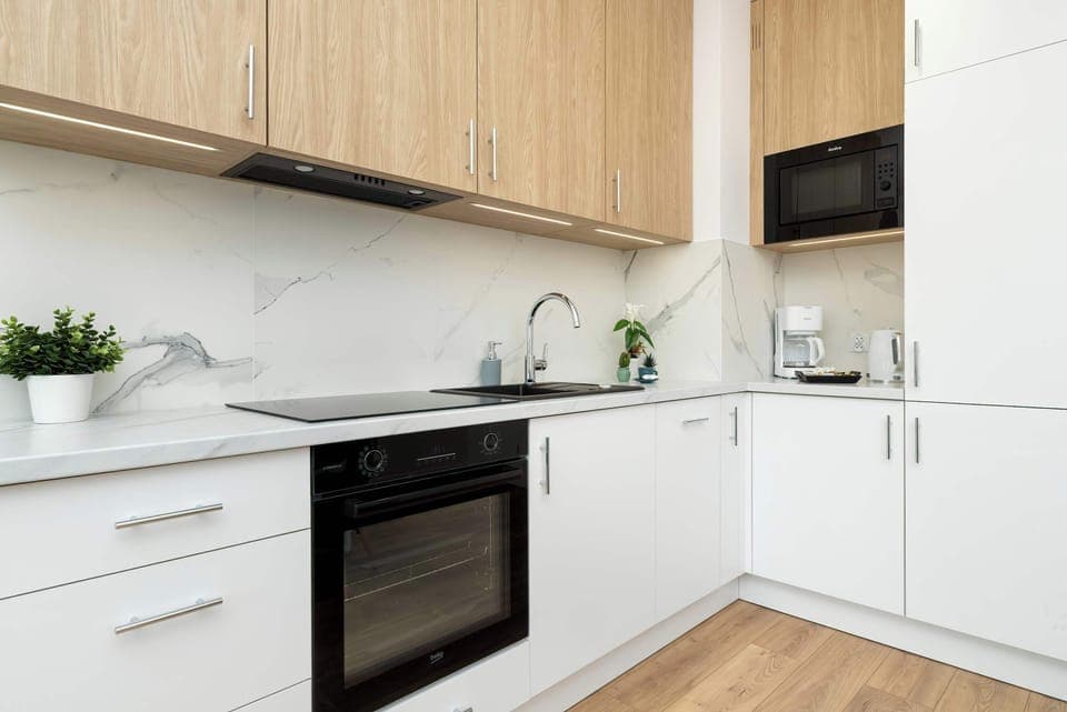 Sleek and functional kitchen space with built-in appliances and natural wood cabinetry. The clean design ensures convenience and style.