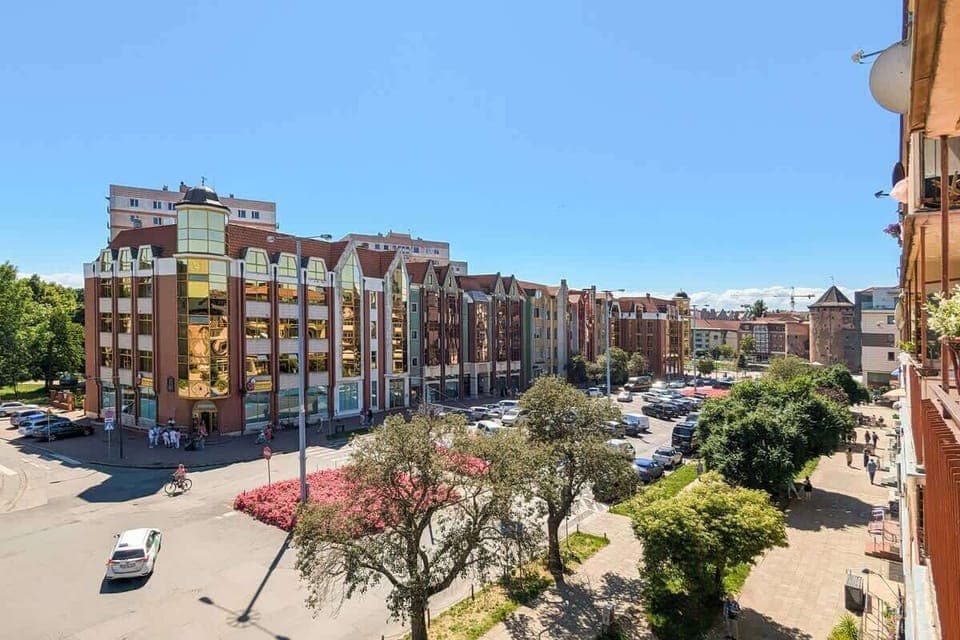 A panoramic view of a city street lined with brick buildings and parked cars.