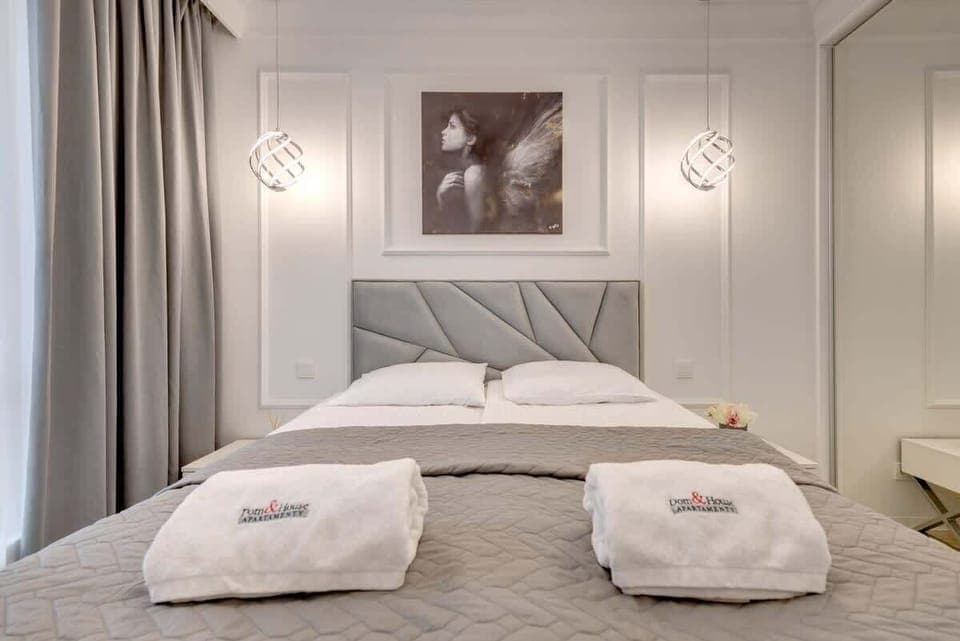 A neatly made bed with a geometric-patterned grey headboard, flanked by modern pendant lights and a stylish monochromatic portrait above, creating a sophisticated bedroom atmosphere.