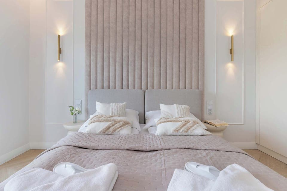 A cozy and elegant bedroom featuring a large double bed with a soft beige headboard and ambient lighting. Minimalist decor creates a calm and relaxing atmosphere.