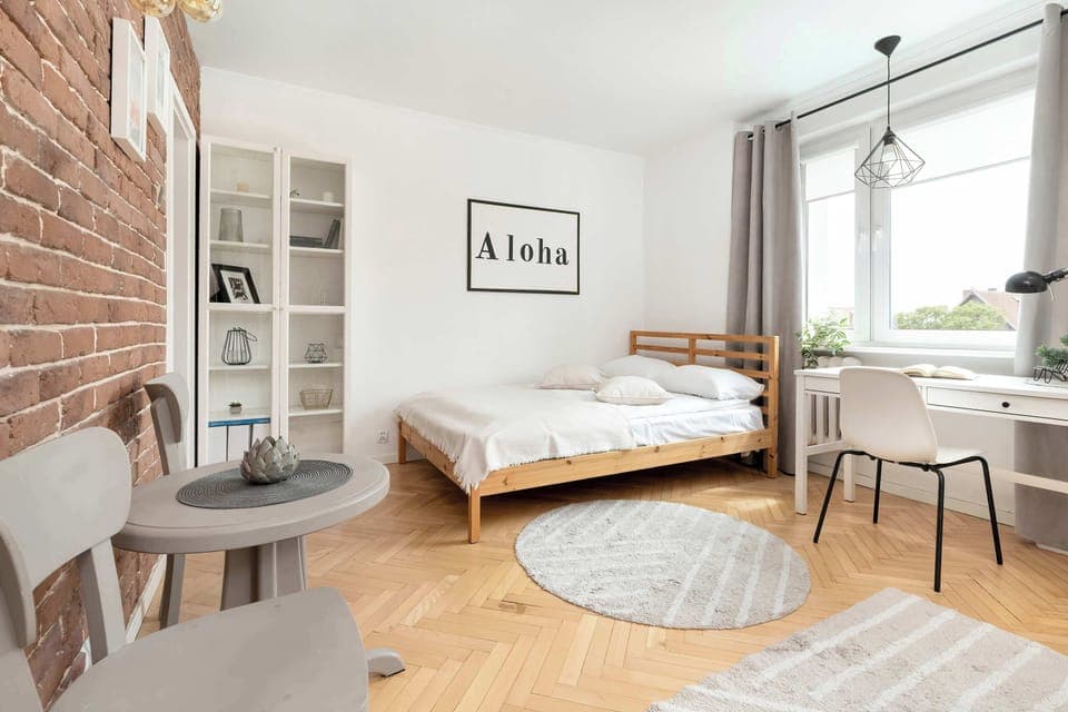 A bright, airy bedroom with one double bed, a round rug, and large windows letting in natural light.