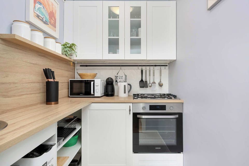 A clean, modern kitchen with white cabinets, a stove, and various appliances neatly arranged on the counter.

