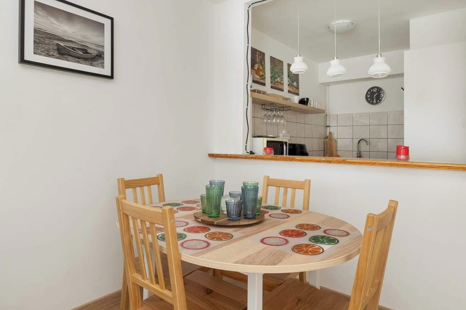 A dining area with a wooden table and four chairs situated next to a small pass-through window looking into the kitchen.