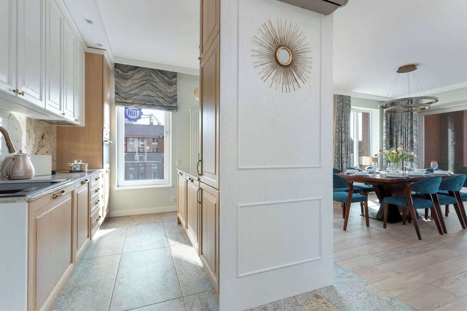 A modern kitchen with built-in appliances, light wood cabinets, and a geometric tile floor.

