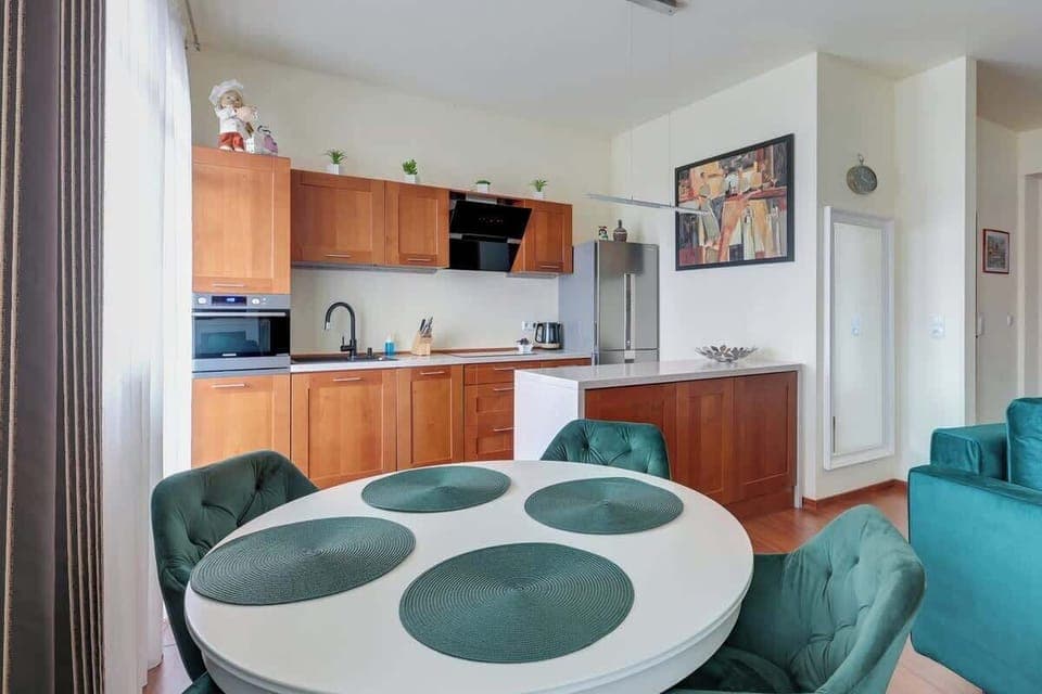 A modern kitchen with wooden cabinets, an oven, and a dining area with a round glass table and chairs.