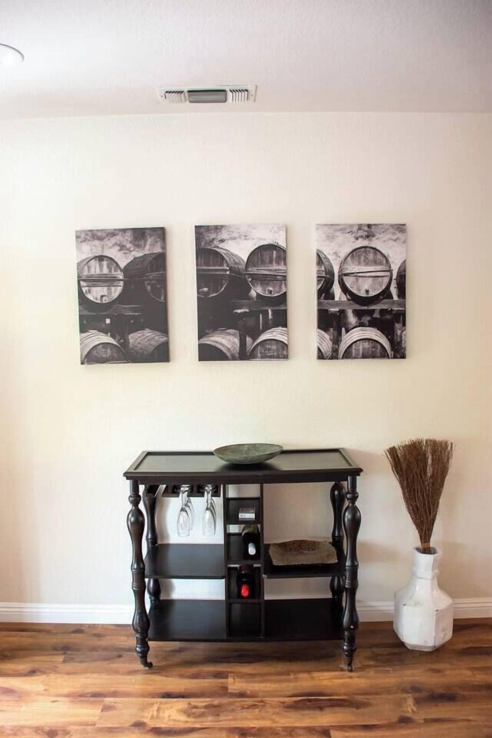 The rich wood flooring enhances the home's decorative flow. This stylish accent table serves as a functional bar area with storage for wine and glasses. The warm, inviting atmosphere is set by the rustic broom detail and the unique artwork above.