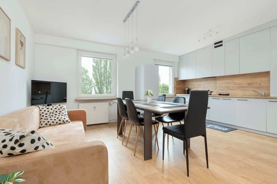 The spacious living room with modern furniture and a large window flooding the space with natural light creates a bright and welcoming area for relaxation.