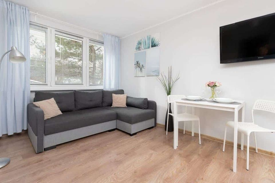 A bright living area with a grey sofa, a white coffee table, and a TV mounted on the wall, creating a cozy space.
