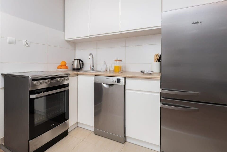 A modern kitchen equipped with white cabinets, a refrigerator, an oven, and other appliances for convenience.
