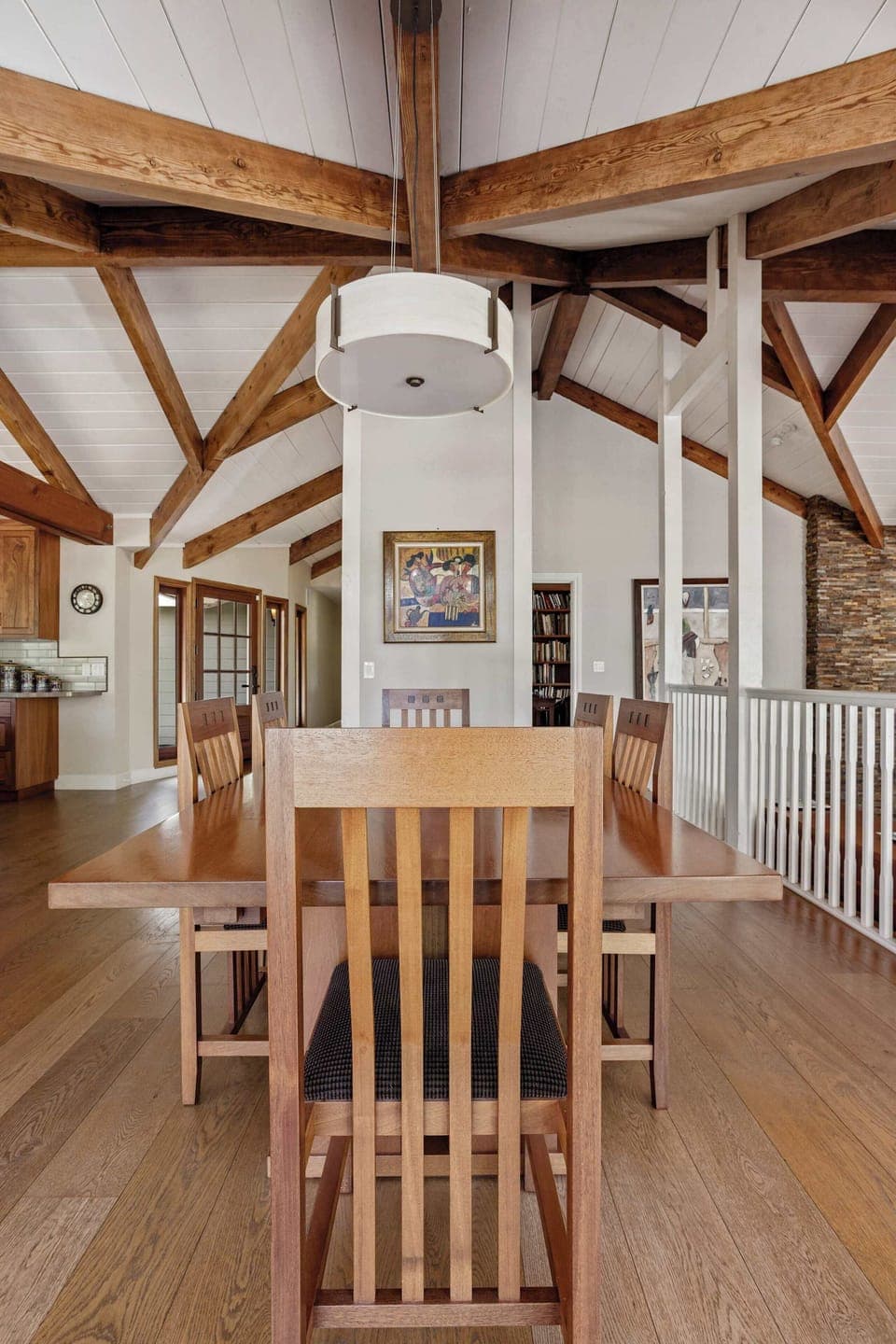 Inviting dining area with a wooden table and chairs, set under vaulted ceilings and exposed wooden beams, next to a decorative white partition wall.