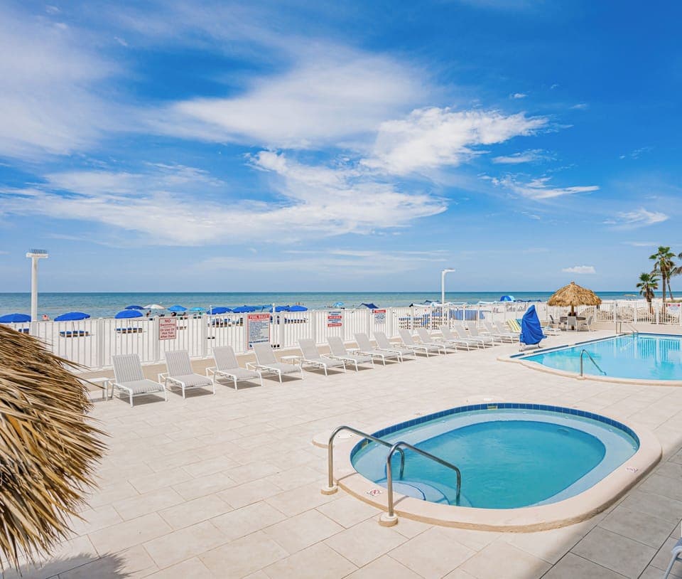 Beachfront pool deck with hot tub overlooking pristine white sand and turquoise waters.