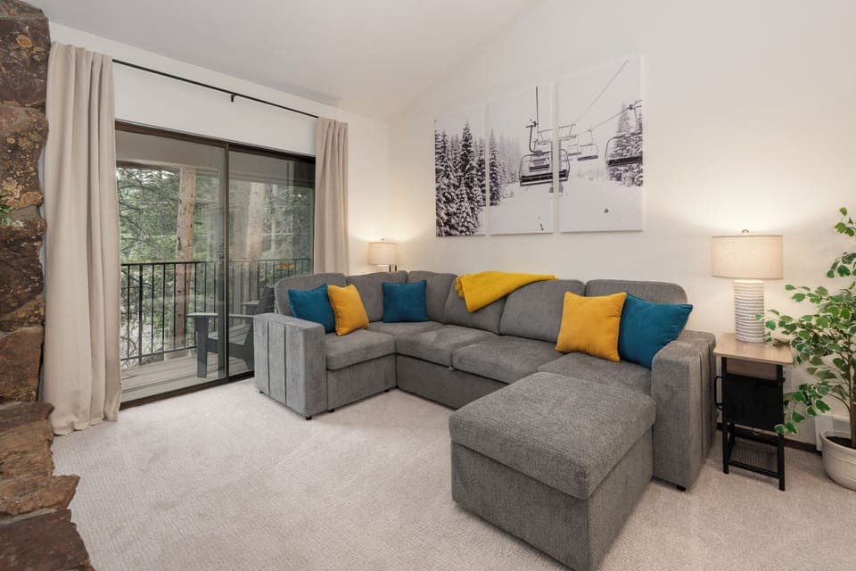 Sink into your cozy sectional sofa where vibrant pillows invite relaxation after mountain adventures, while natural light streams through your private balcony door.