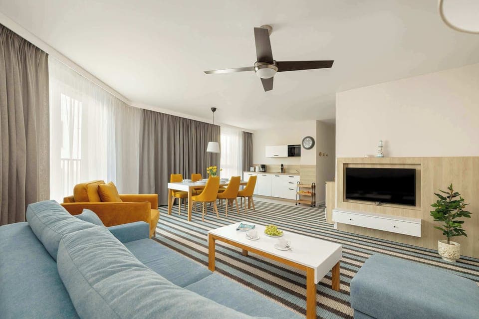 An apartment with a spacious living room, large windows and elegant decor, ideal for a relaxing stay. The interior is bright and cozy, with comfortable furniture and stylish accessories.