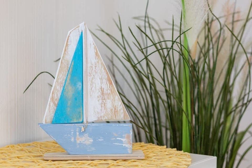 A close-up of a decorative sailboat model placed on a wooden shelf with plants nearby.