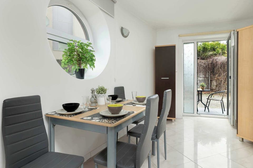A dining area with a set table for four, white tiled floors, and a glass door leading outside.