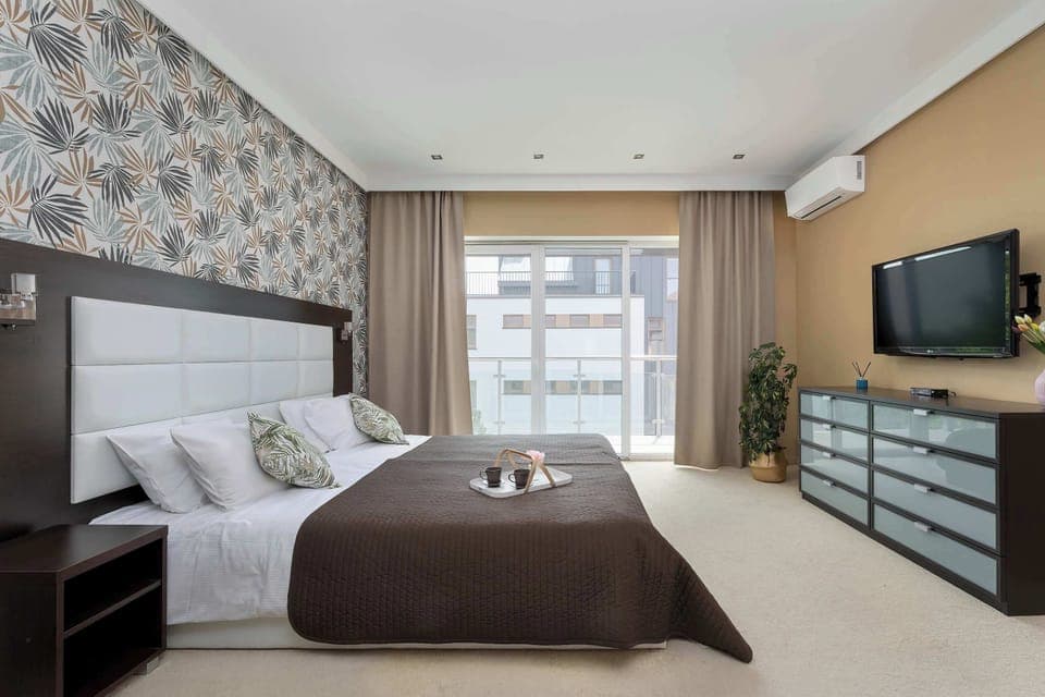 A bright bedroom with a double bed, two bedside tables, and a large window letting in natural light. A cozy space for restful sleep and relaxation.