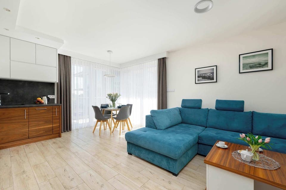 Spacious living room with kitchenette fully equipped, and next to it a blue sofa bed and a wooden coffee table. 