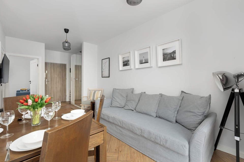 A cozy living room space with a gray sofa, a wooden dining table, and soft lighting. Perfect for relaxing or sharing meals with family and friends.