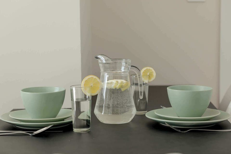 A stylish table setting with green cups, a glass jug, and a modern aesthetic. The decor is simple yet elegant.