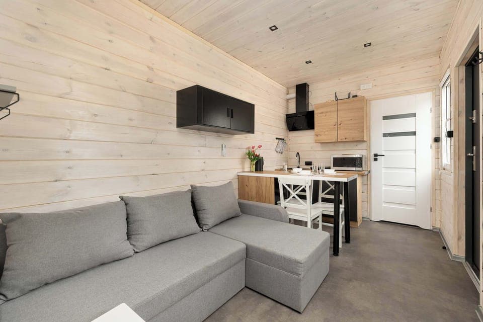 Living area with gray L-shaped sofa, wall-mounted TV, and open access to the dining space.