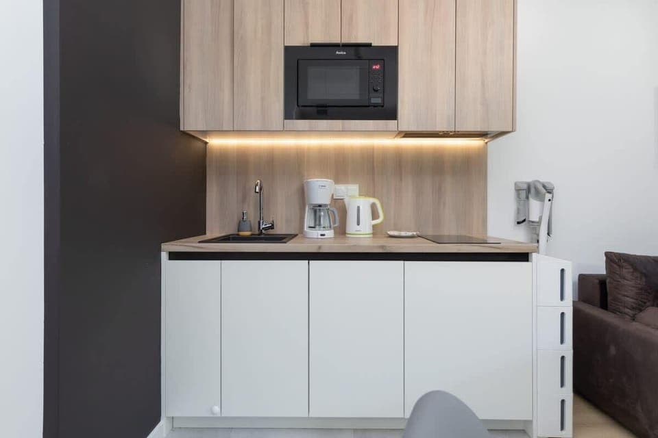 A modern kitchen with white cabinets, a wooden backsplash, and essential appliances, including a microwave and kettle.


