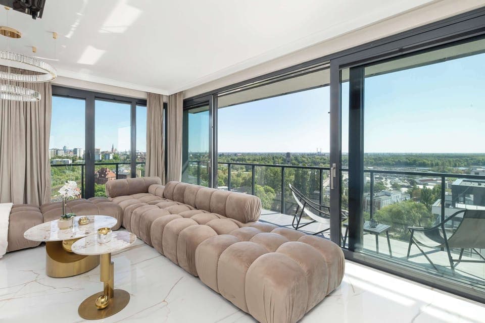 The spacious living room impresses with large windows that let in plenty of natural light, bright walls and elegant furniture, creating a modern and cozy space with a picturesque view of the city.