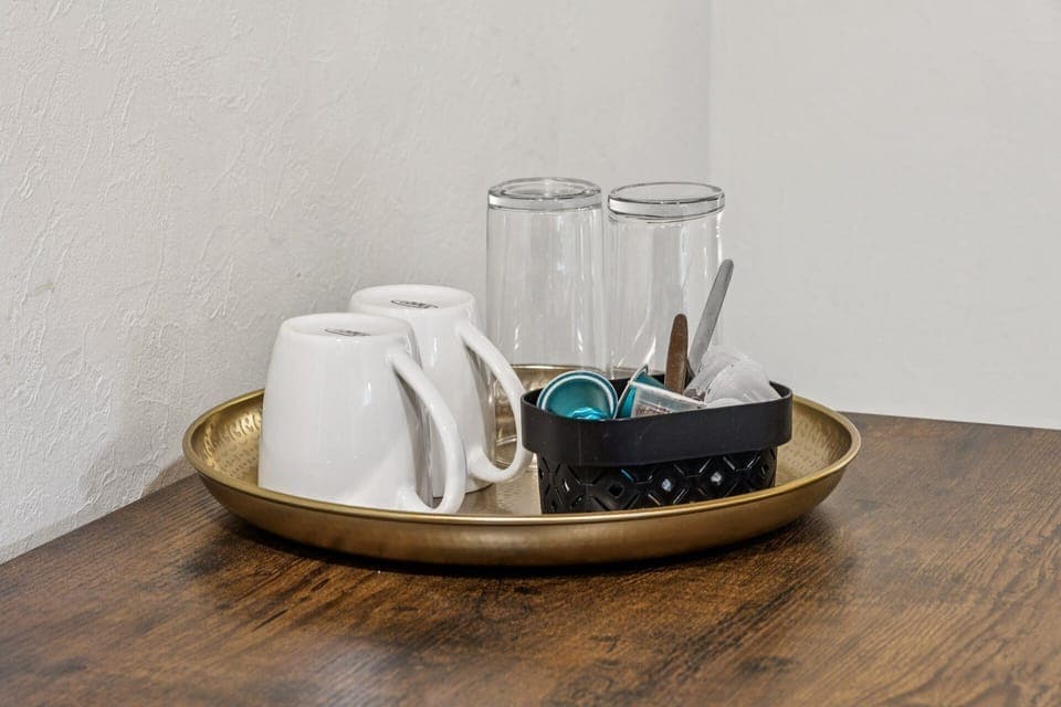 Detailaufnahme mit zwei Tassen, zwei Gläsern und Kaffeekapseln auf goldenem Tablett – kleines Willkommens‑Set für die Ferienwohnung.