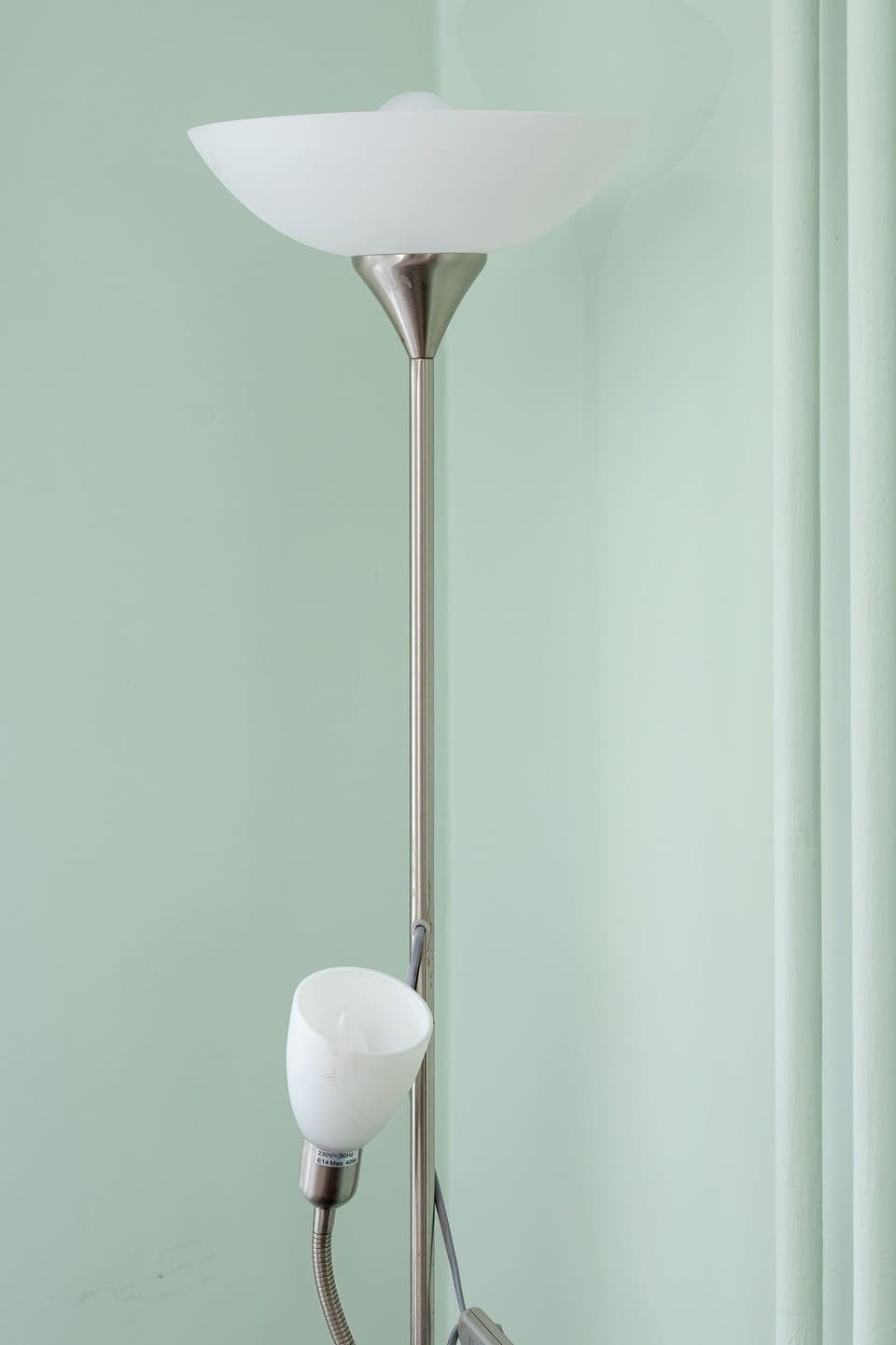 A tall white floor lamp standing against a clean, pastel-colored wall.