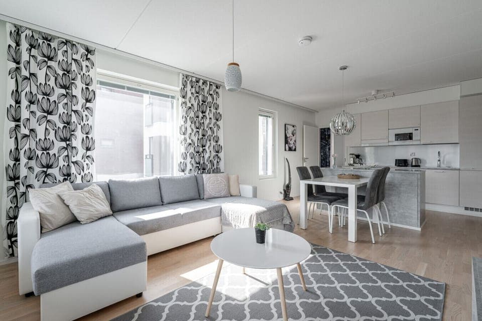 A bright and modern open-concept living space with a cozy corner sofa, fully equipped kitchen, and dining area—perfect for relaxing or entertaining.