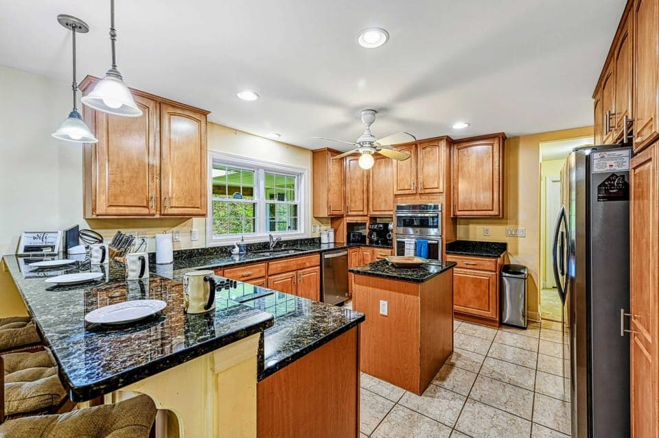 Kitchen - Pendant lights over the breakfast bar with maple cabinets, wall ovens, and stainless refrigerator.